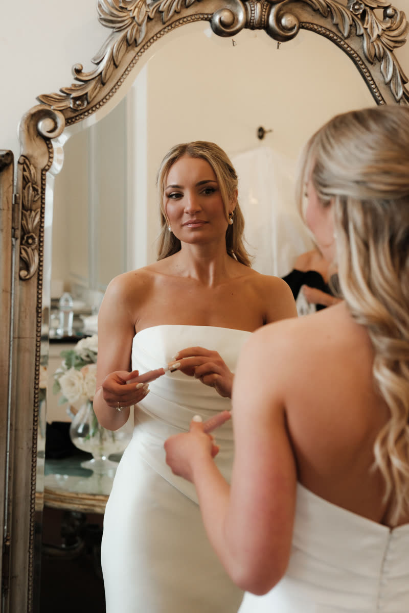 Bride checking her soft, natural wedding makeup in an antique mirror